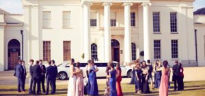 Students in prom dresses gathering outside Hylands House with a white limo in the background.