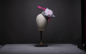 A mannequin head wearing a pink and grey fascinator.