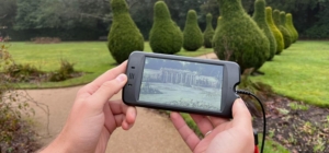 A History Tour handset being held up to the camera with the Pleasure Gardens in the background.