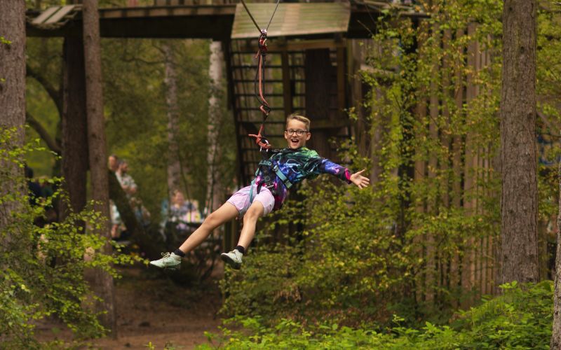 A boy smiling with his arms spread wide while ziplining.