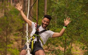 A man smiling, holding his arms up while ziplining.