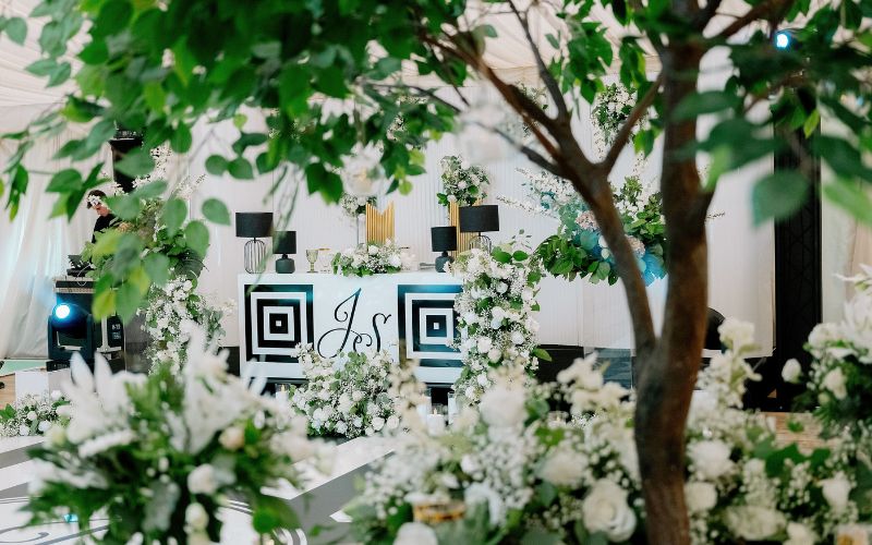 Wedding decorations in the Grand Pavilion featuring colours of gold, emerald green, and black. There are white flowers and leafy trees filling the space.