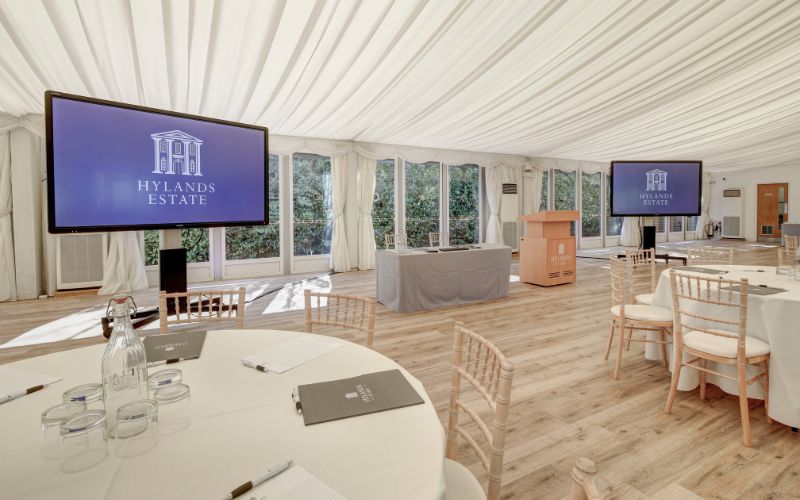 The Grand Pavilion set up for a business meeting with large round tables and podium with two large screens in front.