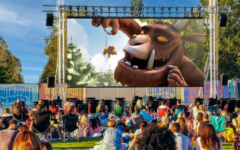 The Gruffalo plays on a large, outdoor cinema screen. The audience is sat on a variety of lawn chairs and blankets.