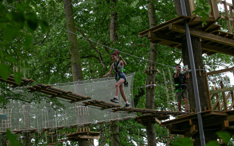 A girl walking across a wood and rope bridge in the treetops.