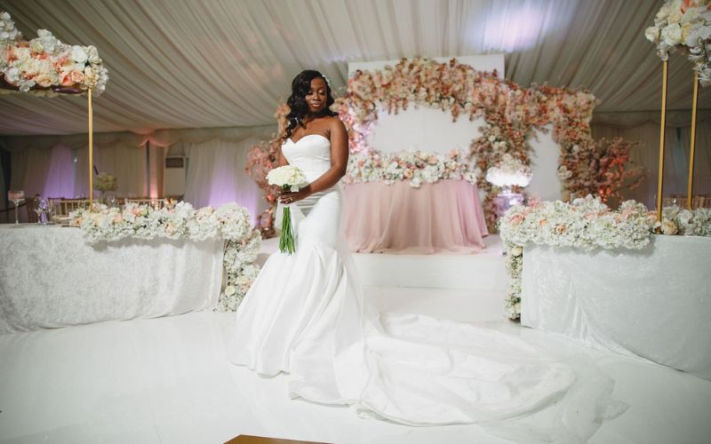 A bride in a long, white dress holding flowers and posing in front of reception décor.