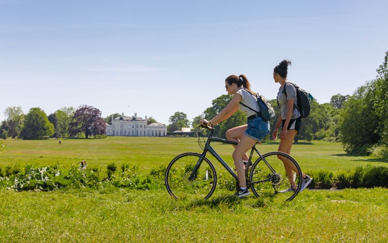 A bicyclist and walker in the fields of the Estate with Hylands House in the background.