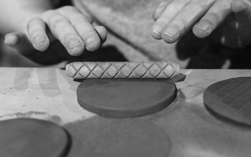 A closeup of someone rolling a pattern into circular clay.