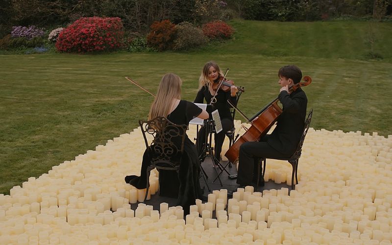 A string trio playing on a stage surrounded by LED candles.