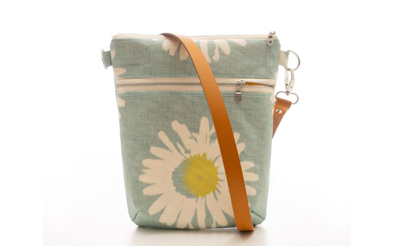 A shoulder bag with a brown leather strap and daisies.