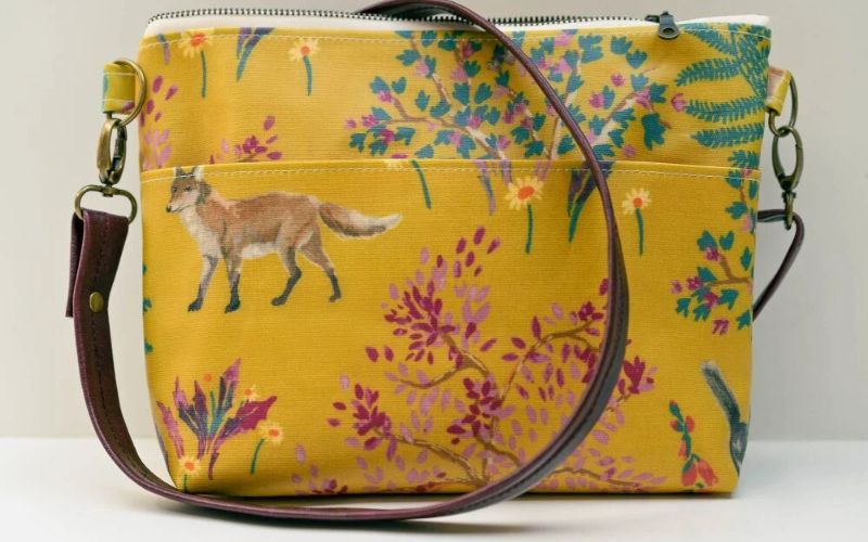 A yellow shoulder bag featuring various plants and a fox.