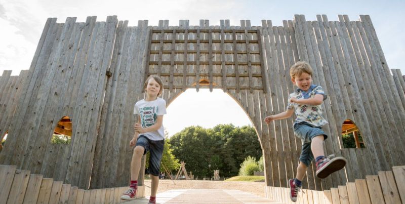 Two young boys run through the wooden gate entrance to the Adventure Castle play area.