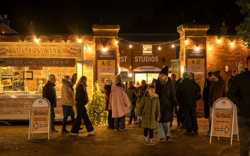 A crowd of people outside the walls of The Stables with Christmas decorations and a snow machine.