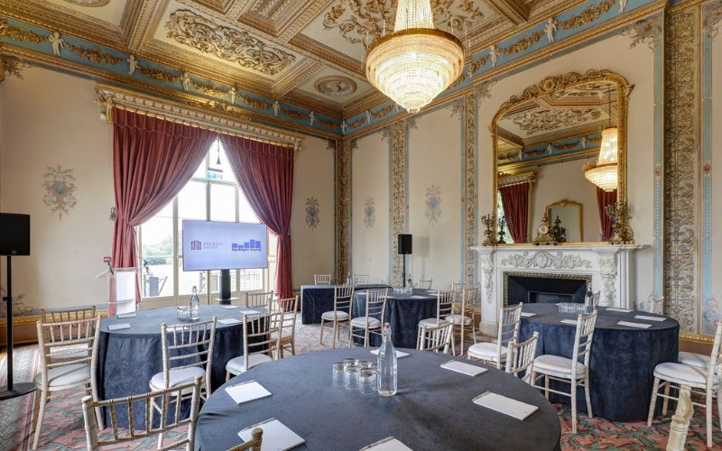 The Drawing Room set with round tables and a large screen at the front. The celling is ornately decorated with gold and teal accents.