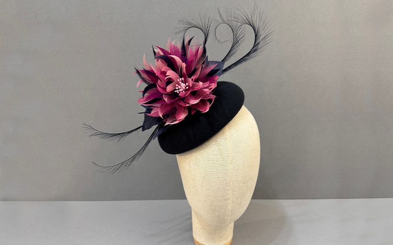 A black and pink hat featuring a large flower and wispy feathers.