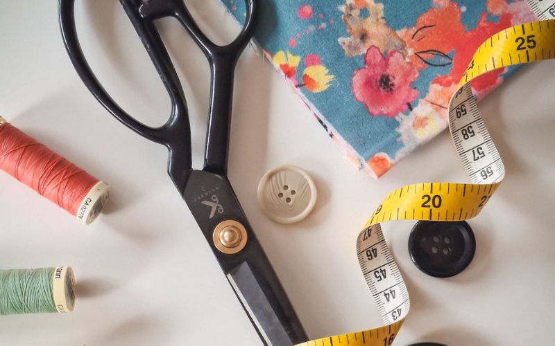 make do and mend Scissors, thread and measuring tape laying on a table.