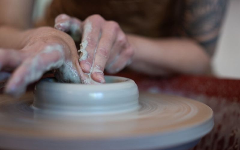 A closeup of hands working with clay on a potter's wheel.