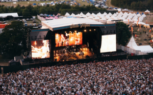 A large crowd standing in front of a big stage with a band playing.
