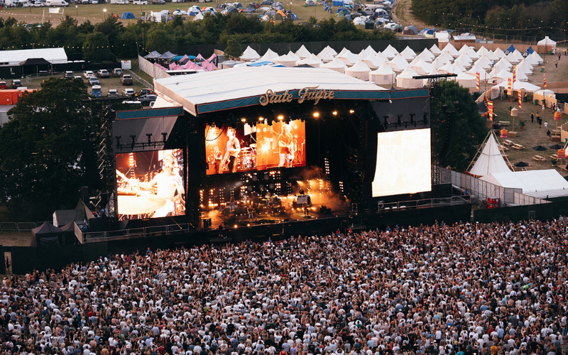 A large crowd standing in front of a big stage with a band playing.