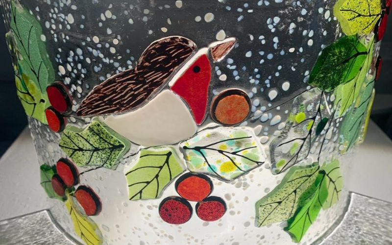 A glass decoration featuring a robin on holly leaves.