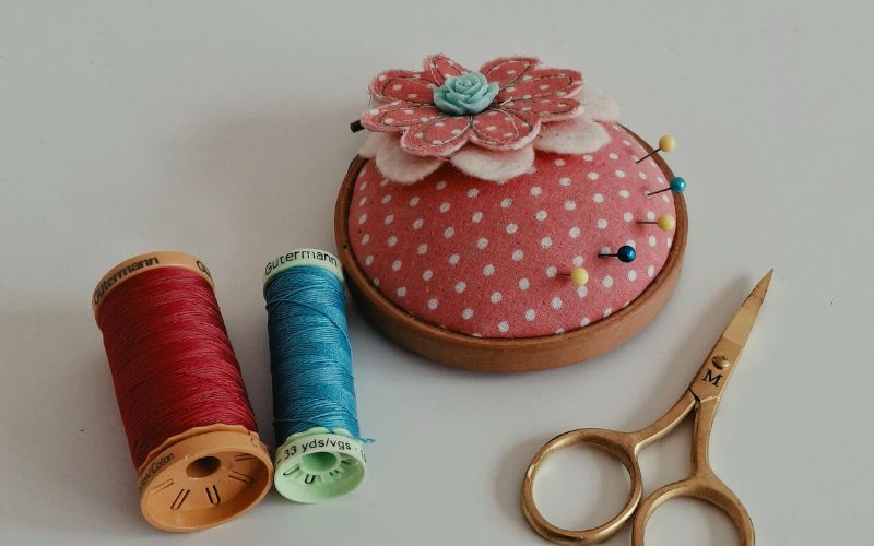 A red polka dot pincushion decorated with a fabric flower.